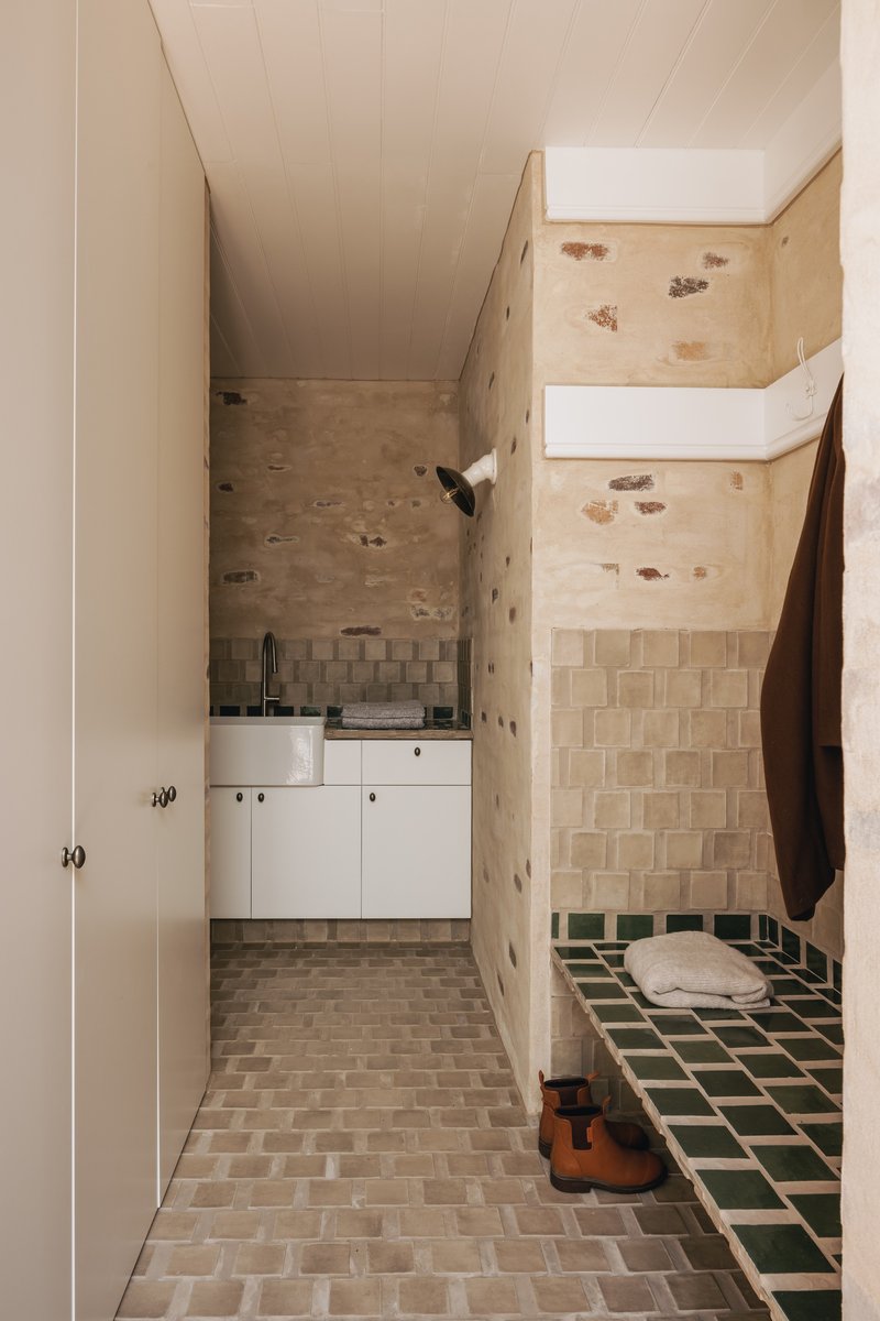 Compact bathroom with exposed stone walls, beige tile floor, green tiled bench, and skylight above