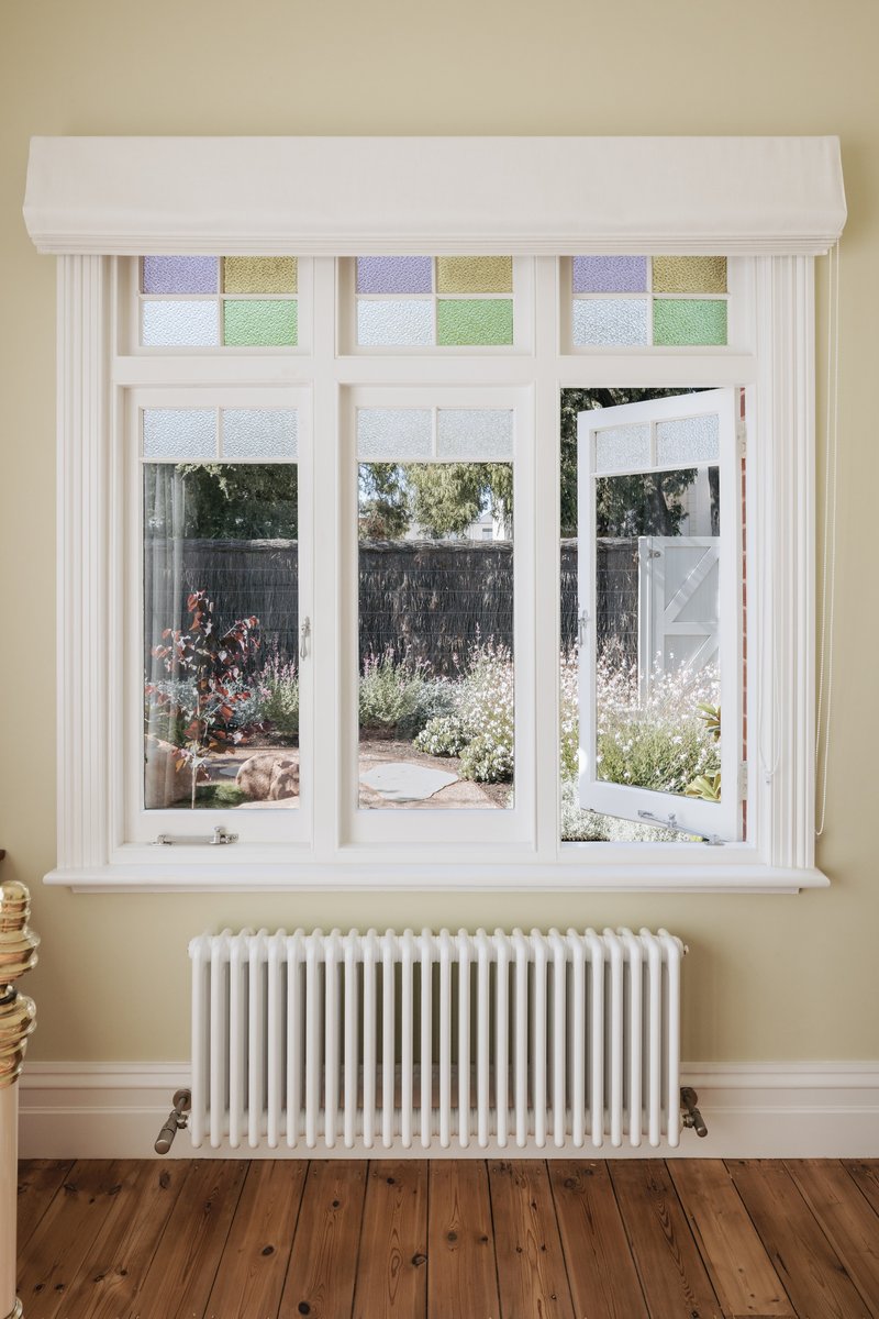 White timber window with colored glass transom panels overlooking a garden with flowering plants
