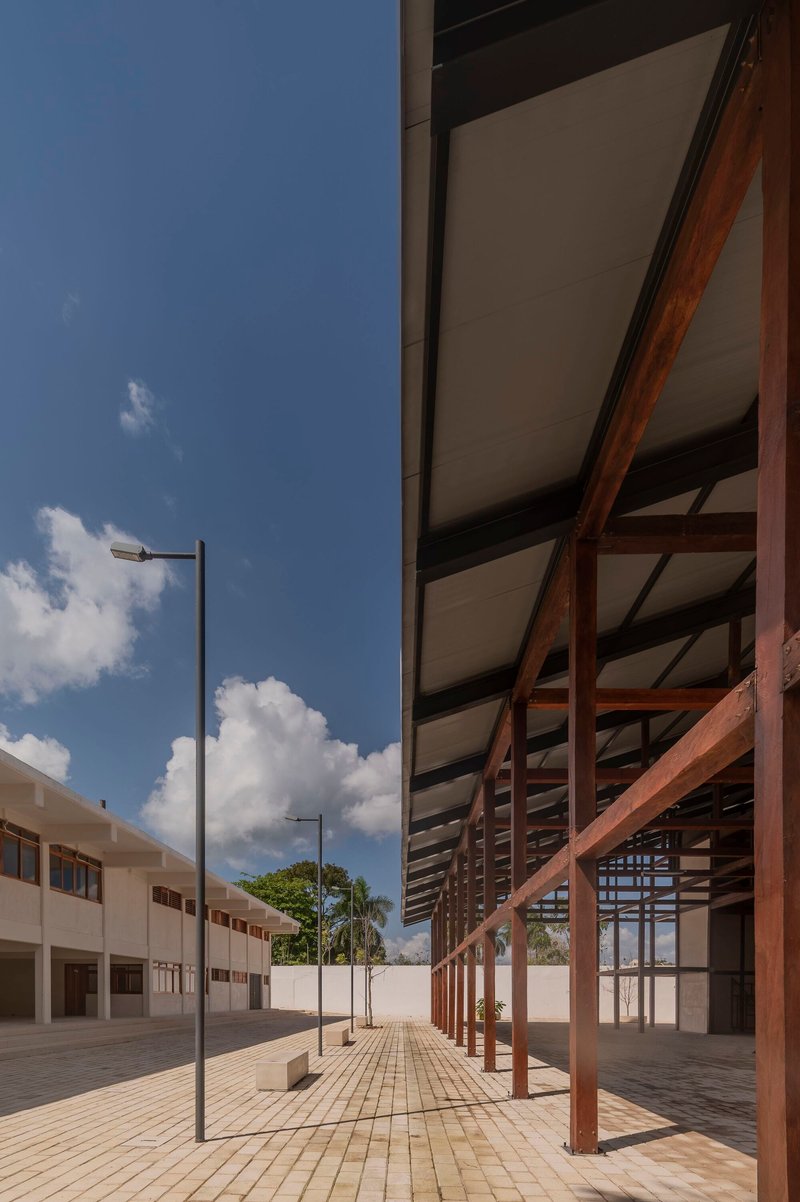 Timber colonnade with diagonal bracing and pale ceiling panels adjacent to a tiled courtyard