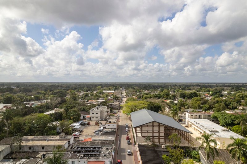 Aerial view of a gabled roof structure with exposed steel framework among low-rise buildings and palm trees