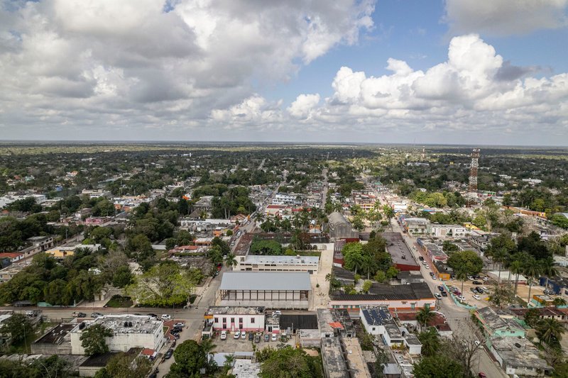 Drone view of the warehouse-style building with expansive glazed facade rising above surrounding neighborhood rooftops under cloudy skies