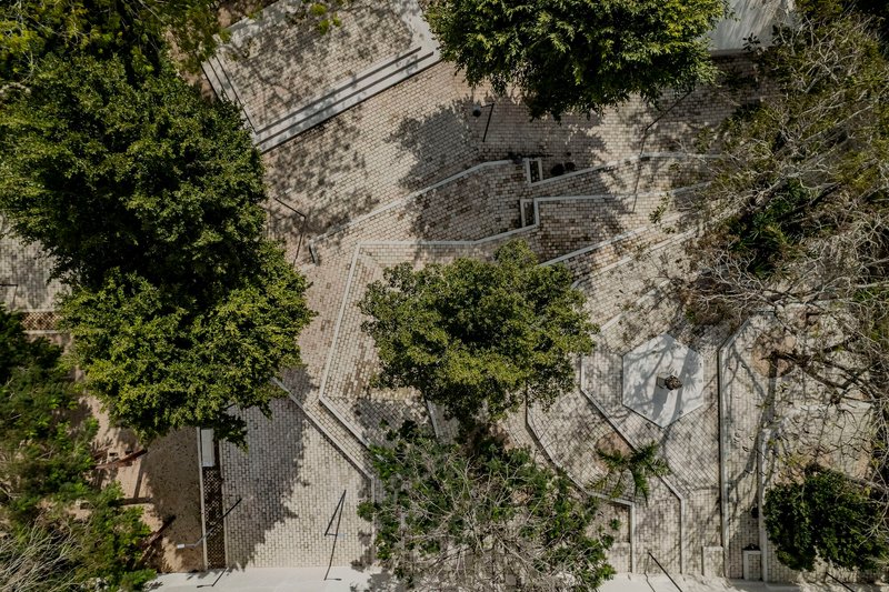 Overhead view of paved plaza with stone pavers, curved pathways, and trees casting dappled shadows