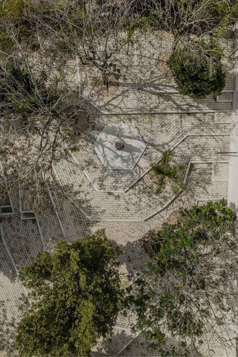 Drone view of stone-paved plaza with diagonal pathways, scattered trees, and a single person walking