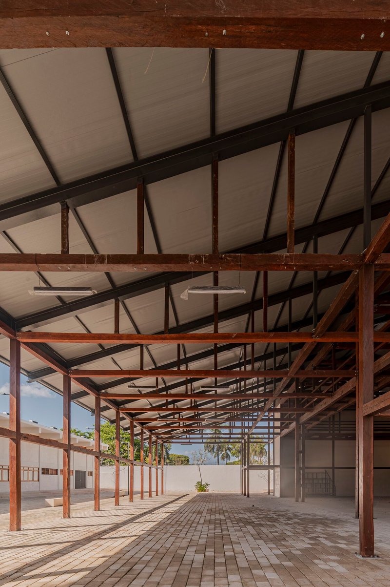 Interior view of the sheltered hall with exposed timber beams and brick floor leading toward planted courtyard