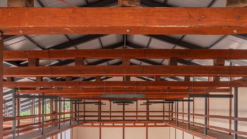 Interior view of layered timber beams and metal railing system beneath a translucent panel ceiling