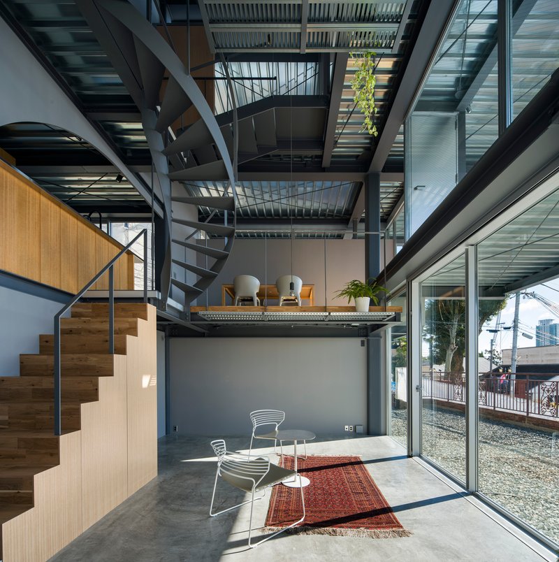 Triple-height interior with spiral staircase and stacked mezzanine platforms beneath a slatted ceiling open to sky