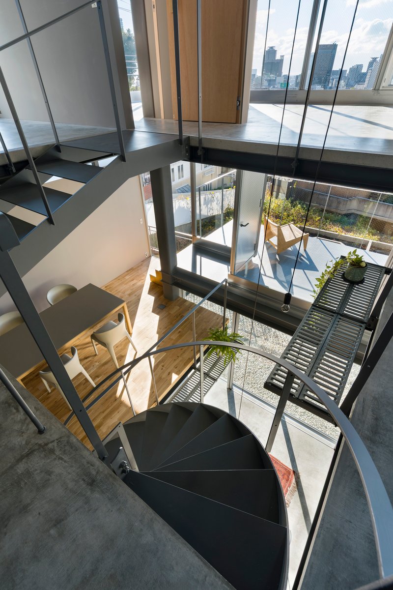 Looking down through the steel spiral staircase into the double-height space with terraced courtyard beyond