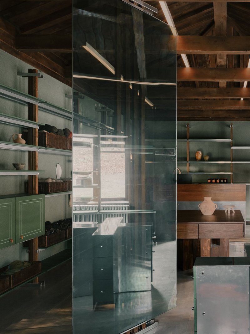 Reflections on translucent glass partition showing timber ceiling structure and green cabinetry beyond