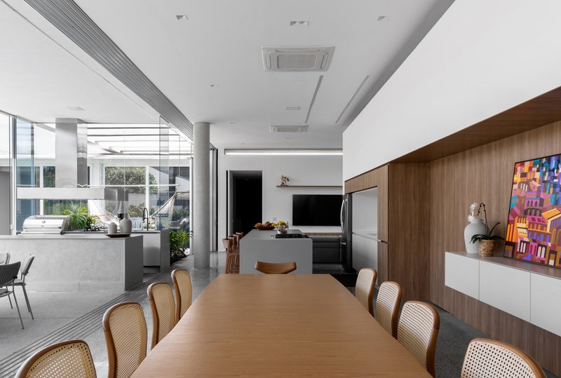 Open-plan dining and kitchen space with walnut cabinetry and cane-backed chairs beneath a white ceiling