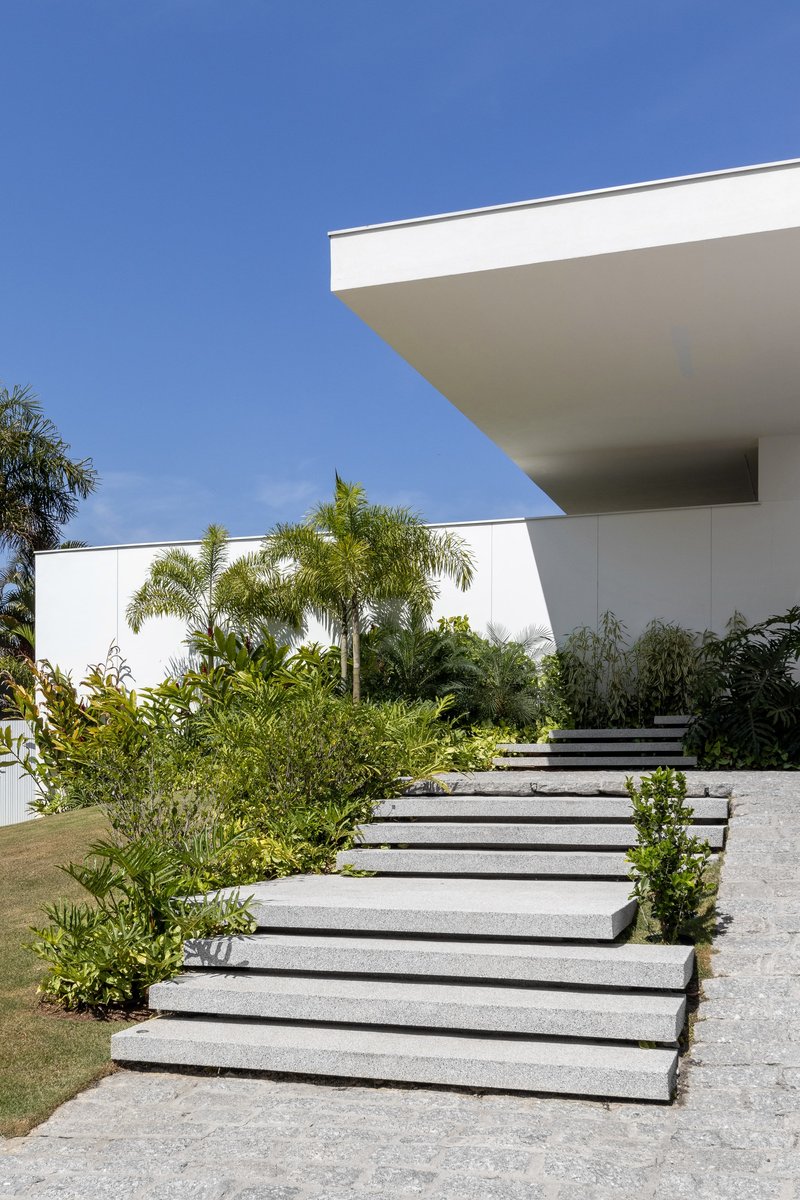 Floating concrete stepping pads rising through lawn and planting toward cantilevered white roof slab overhead