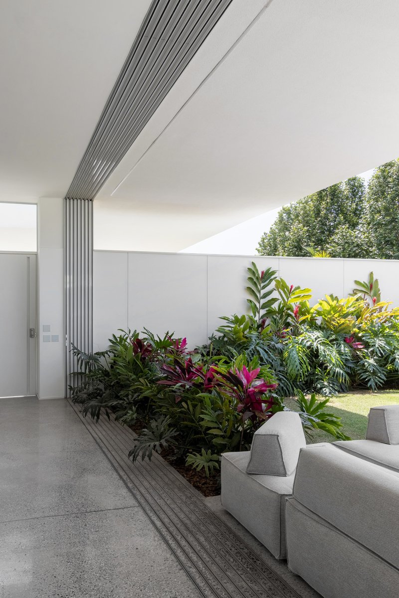 Interior courtyard with linear metal louvres meeting a planted bed of tropical foliage along the wall