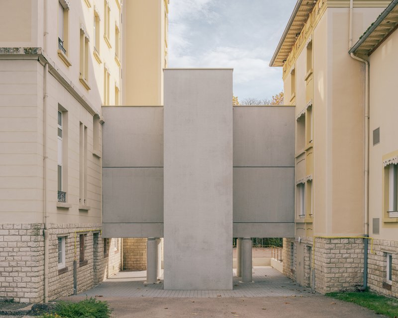 Courtyard view of stacked grey concrete panels raised on brick bases between plastered heritage wings