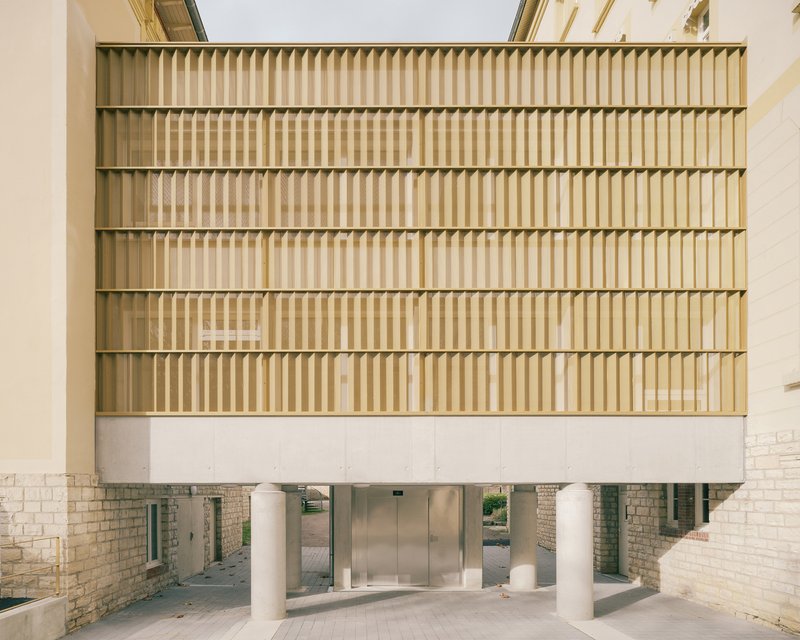 Head-on view of horizontal timber louvre facade lifted above a glazed ground floor on white columns