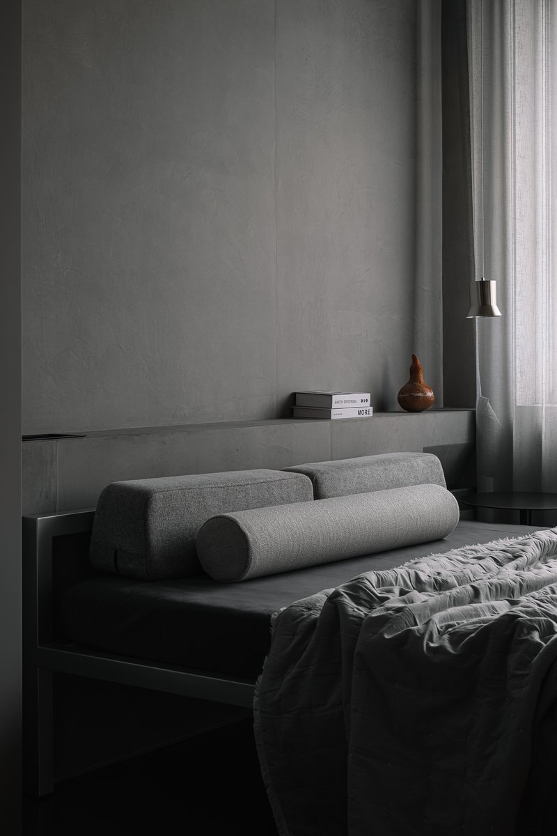 Bedroom with grey concrete ledge, cylindrical bolster cushions, and pendant light beside window
