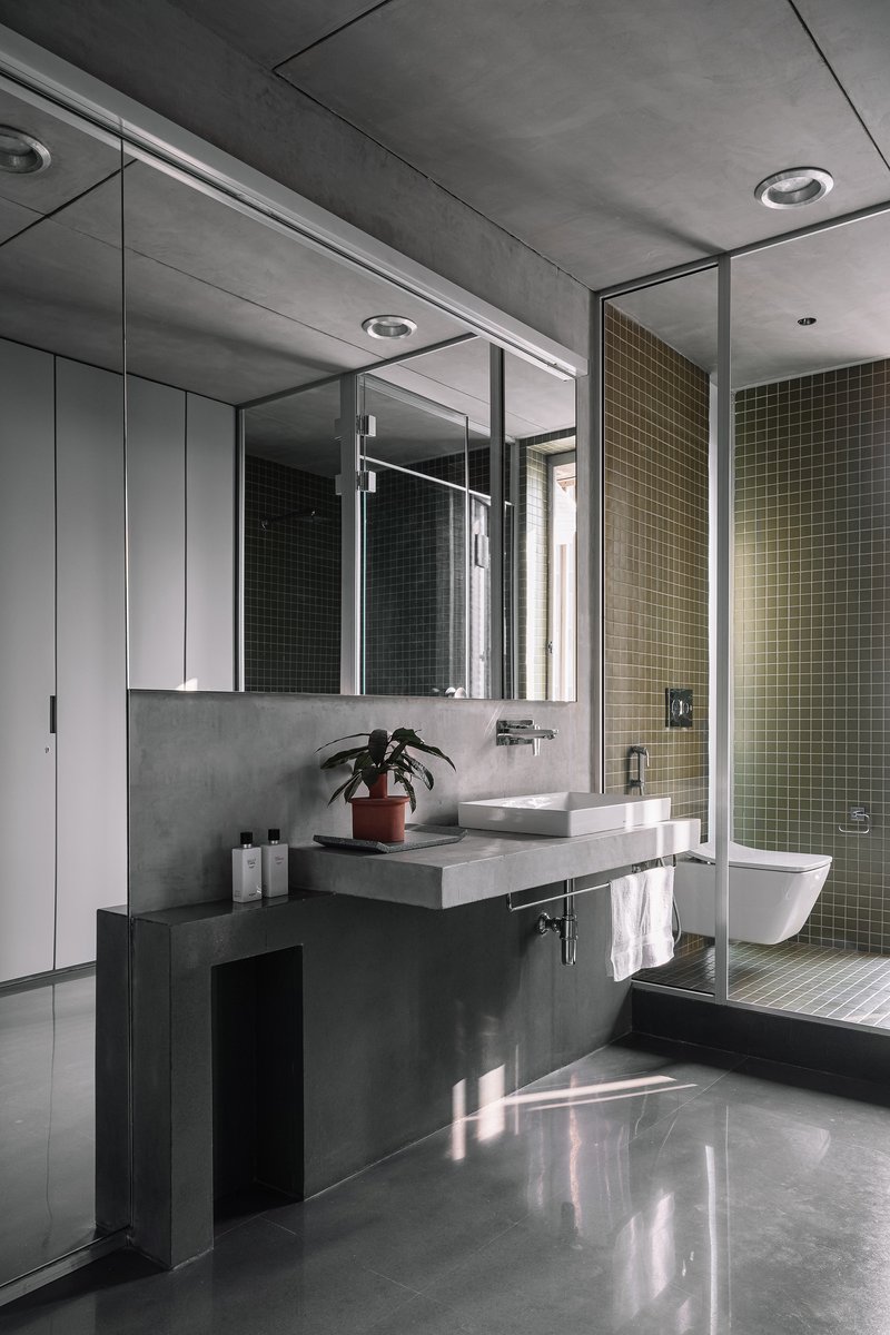 Bathroom with floating concrete vanity and glass-enclosed shower lined with small mosaic tiles