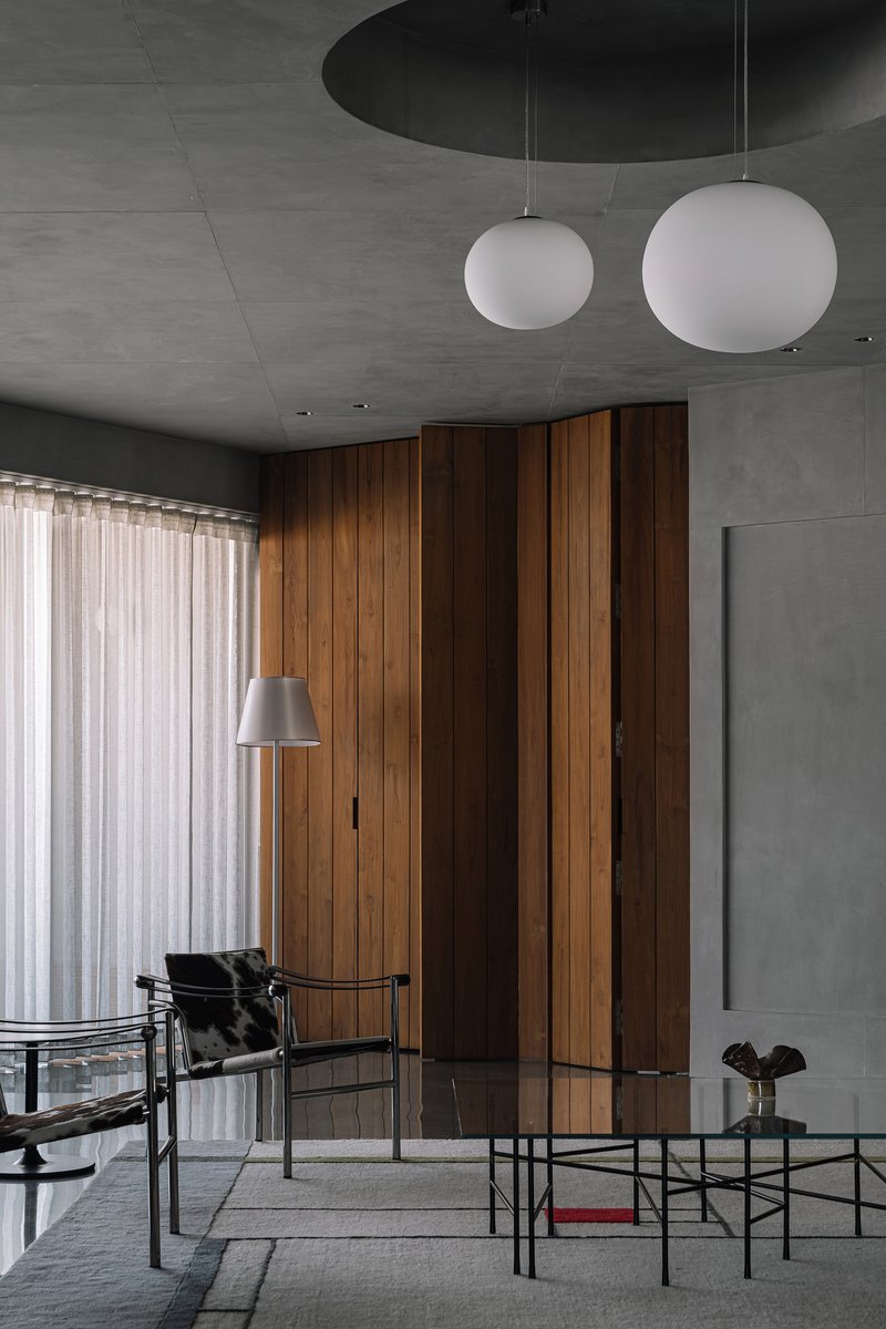 Living space with vertical timber wall panels beneath exposed concrete ceiling and spherical pendant lights