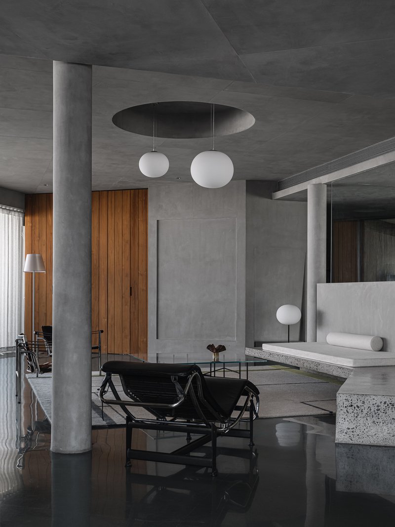 Open living space with circular concrete column and recessed ceiling oculus above globe pendants