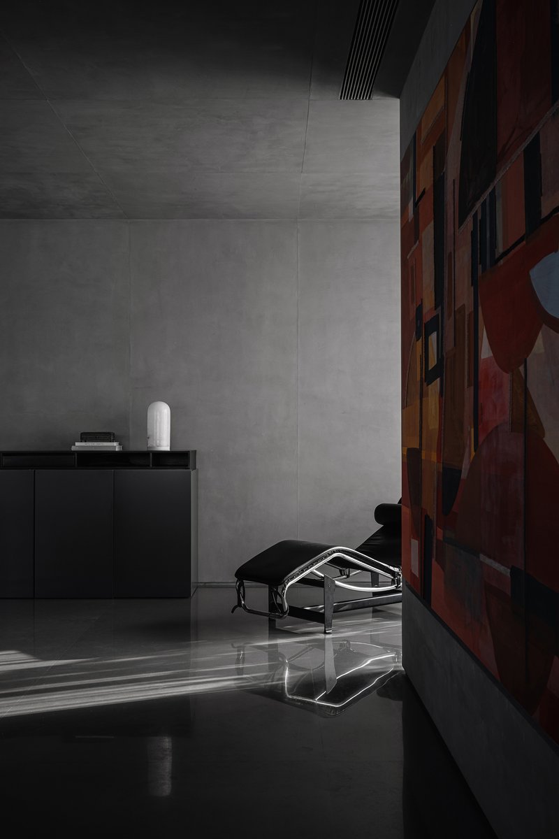 Interior corner with grey concrete walls and a low armchair beside a colorful abstract painting
