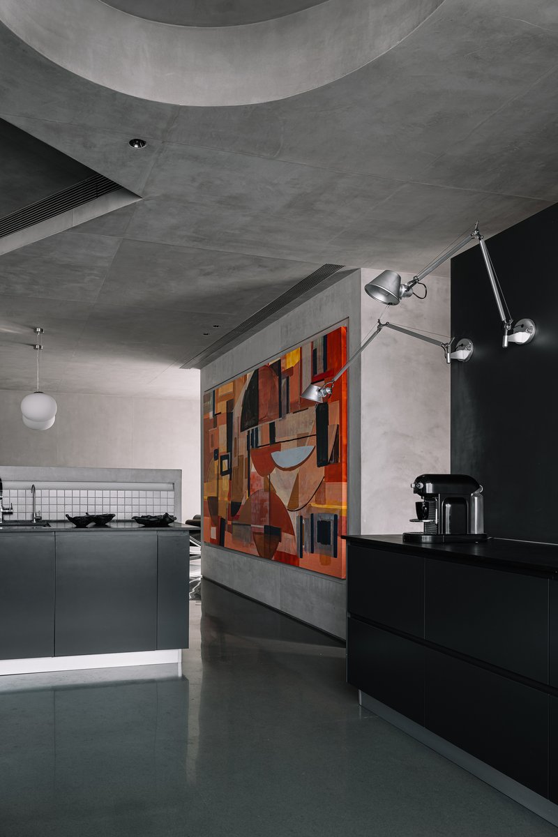 Kitchen area with black cabinetry and colorful geometric mural behind a grey concrete partition wall