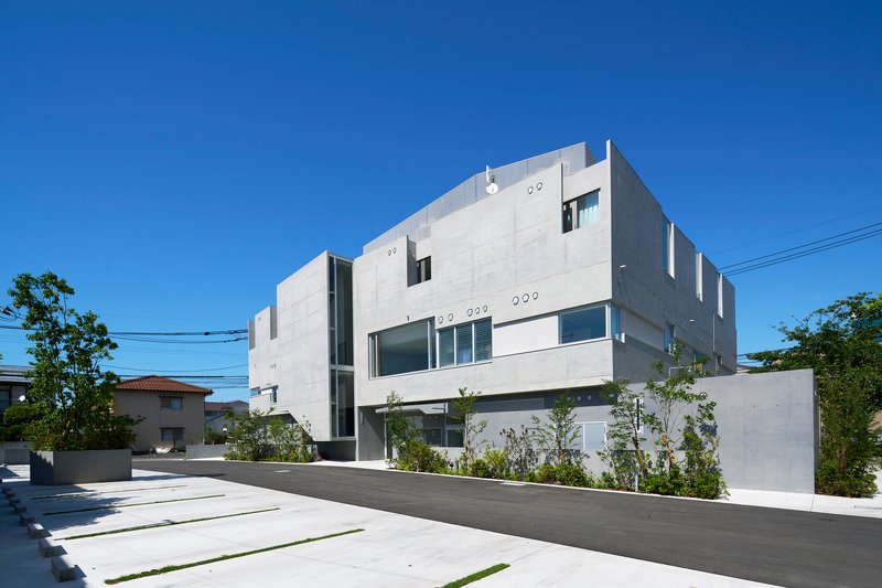 Street view of the white concrete volumes with varied window openings under a clear blue sky