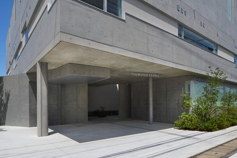 Recessed concrete entrance portico with cylindrical columns and planted bed under clear blue sky