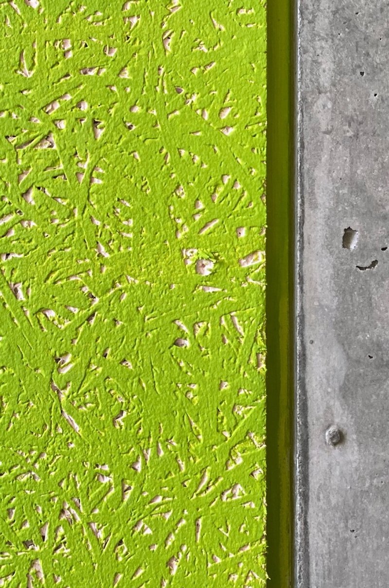 Detail of lime green textured plaster panel meeting raw concrete slab edge with visible formwork holes