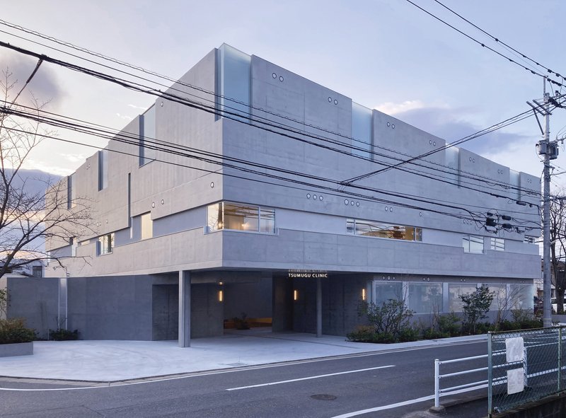 Street view of horizontal concrete panel facade with ground floor glazing and overhead power lines at twilight