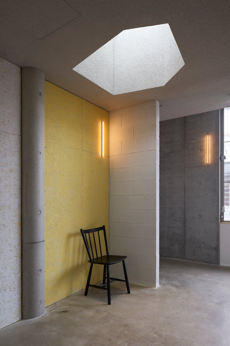 Pentagonal skylight opening in a dark grey ceiling above a yellow acoustic panel and black chair