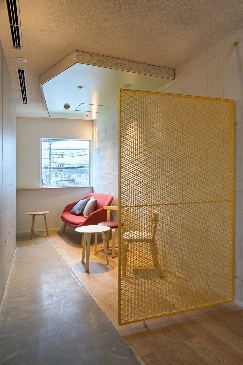 Yellow woven mesh partition enclosing seating nook with pink chair and window