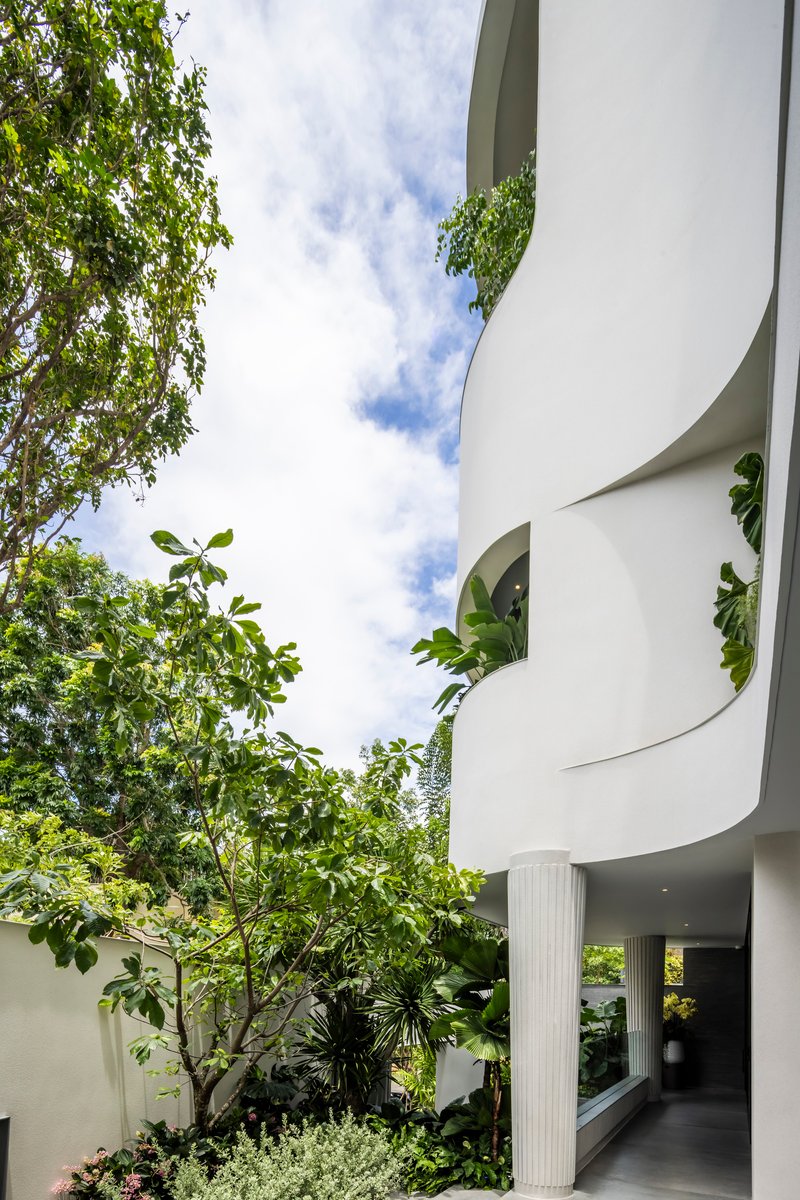 Upward view of spiraling white balconies with planted edges beside a deciduous tree