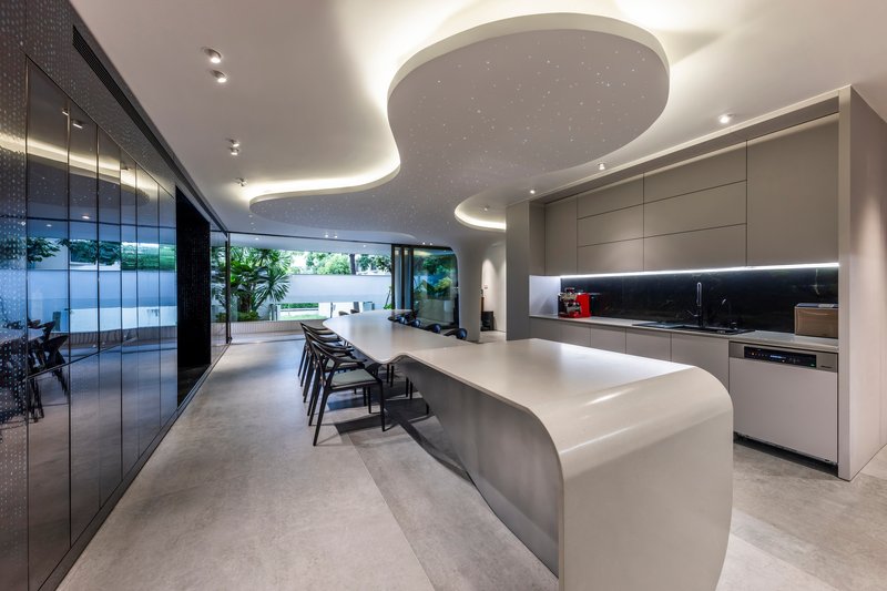 Kitchen and dining space with curved island beneath an organic ceiling cutout overlooking the courtyard