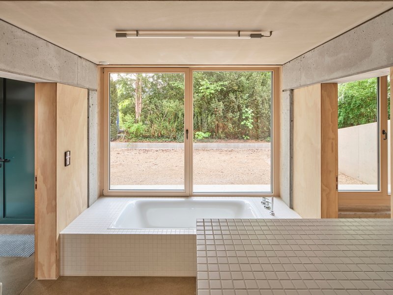 Bathroom with white tiled bathtub platform facing full-height glazed doors to exterior gravel garden