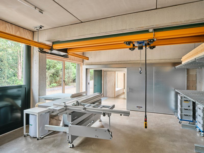 Workshop interior with yellow overhead crane beam and table saw facing plywood-framed glazing
