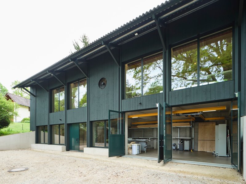 Two-story timber facade with exposed corrugated overhang and open garage doors revealing workshop equipment