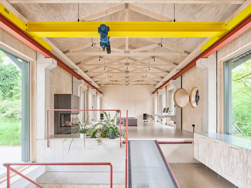 Interior view showing exposed timber truss ceiling with yellow overhead crane beam and plywood walls framing large windows