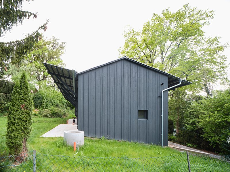 Gabled volume clad in vertical dark grey timber siding with extended eaves and adjacent white utility block