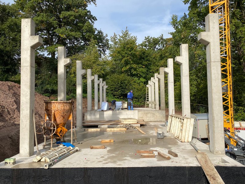 Construction site showing rows of precast concrete columns set into a concrete slab with a yellow crane visible