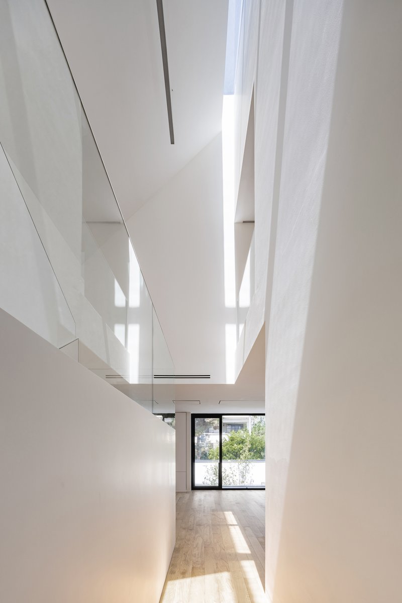 Triple-height skylight shaft with white walls and wood flooring below in bright daylight