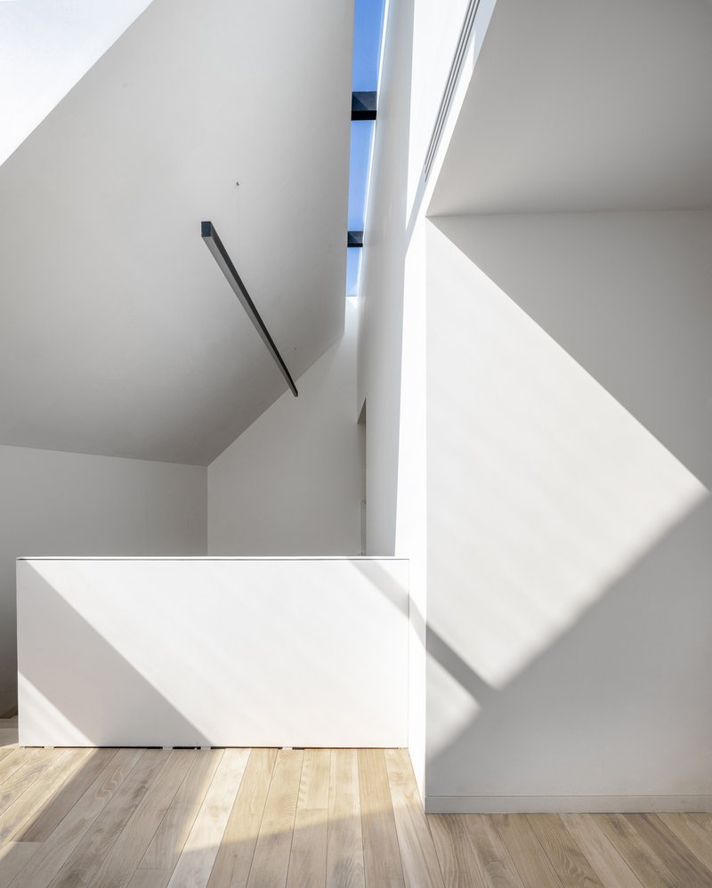 Angled stairwell with black metal handrail and sunlight casting sharp shadows across white surfaces