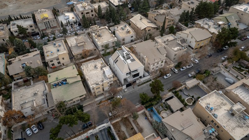 Aerial view of white rooftop volumes surrounded by residential blocks and parked cars