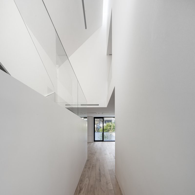 Corridor with angled white walls and skylights leading toward a glazed door with garden beyond
