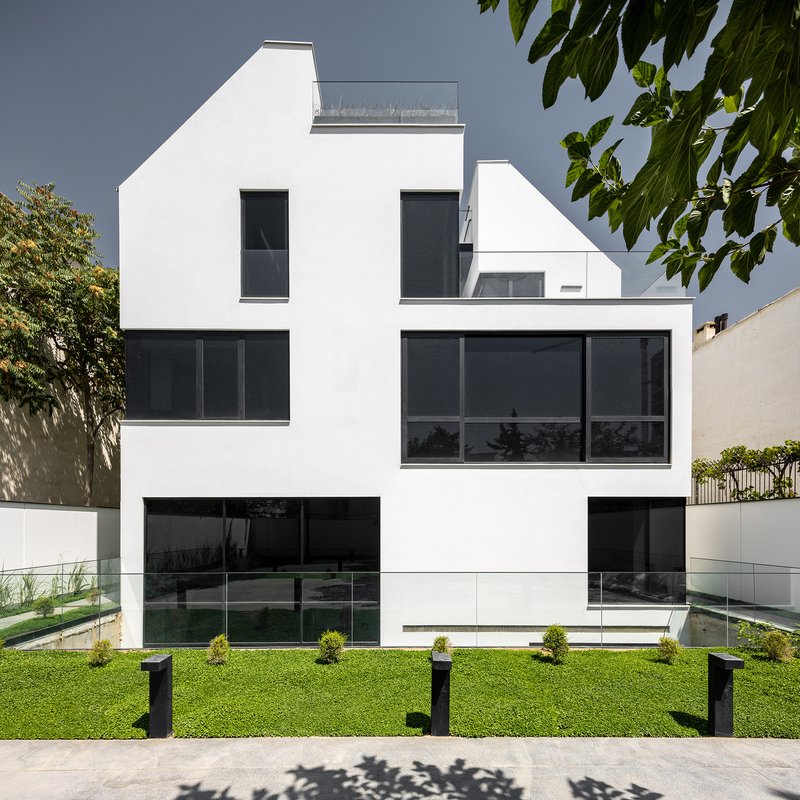 White rendered facade with dark glazing and lawn garden framed by overhanging tree branches