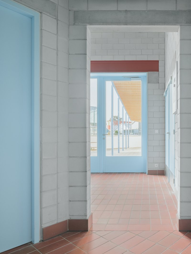 Interior corridor with white tile walls, terracotta flooring and pale blue door framing an exterior porch