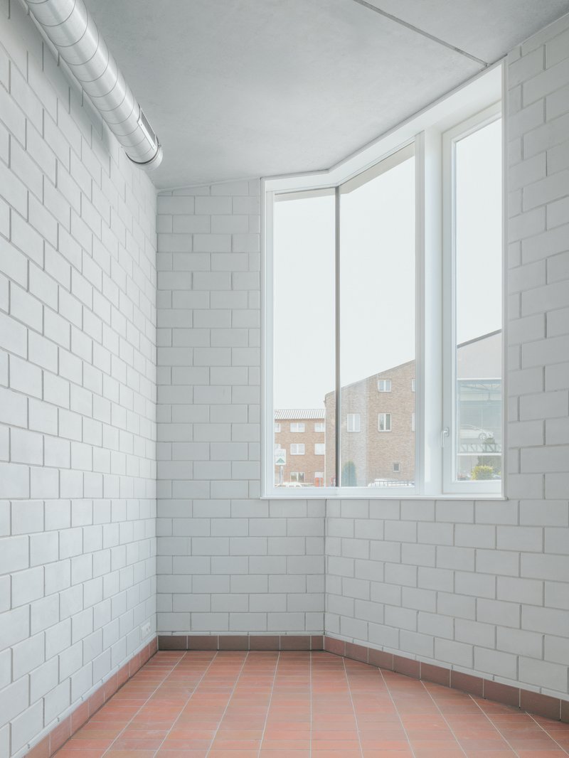 Corner room with white tiled walls, exposed ductwork and corner window overlooking neighboring buildings
