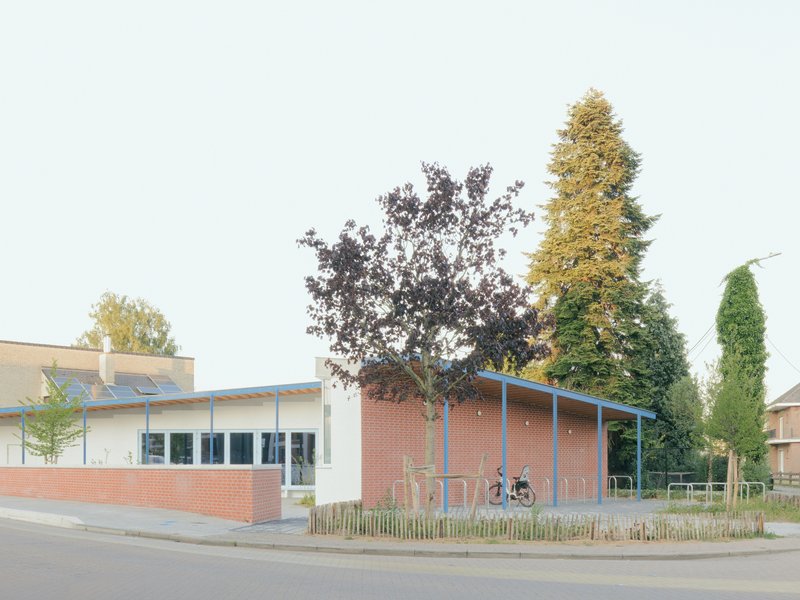 Corner view of the brick and white-rendered building with a curved metal canopy and wooden bike rack fence