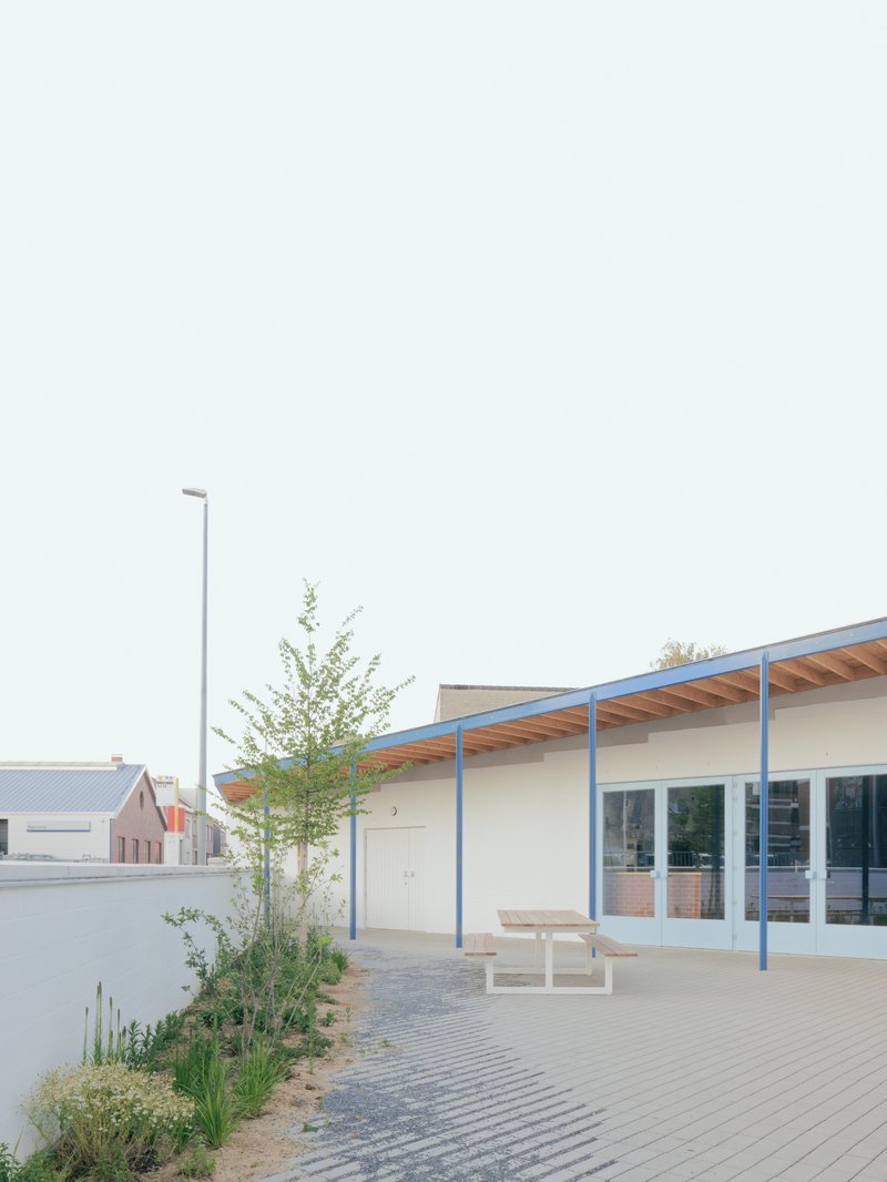 Courtyard with paver surface, timber picnic tables and planted beds beneath the overhanging timber and steel roof