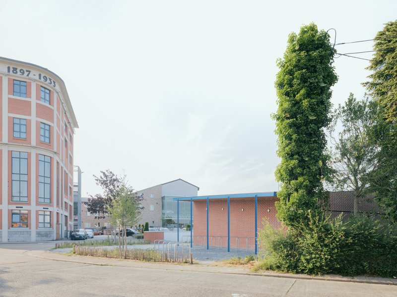 Street view of brick pavilion with blue trim beside curved facade and trees