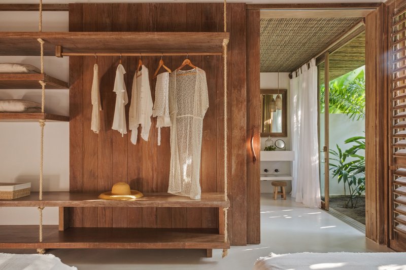 Bedroom closet with rope-suspended bench, hanging garments and view through to ensuite bathroom