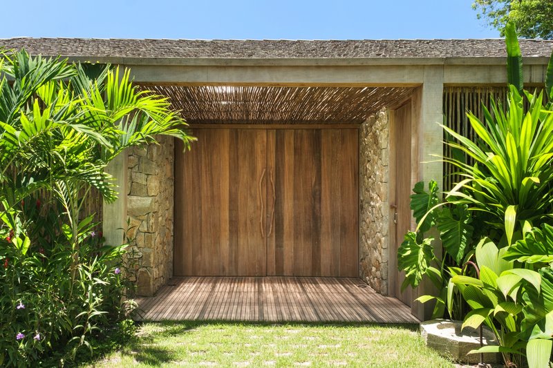 Covered entrance with timber doors, stone walls and woven wood ceiling surrounded by tropical plantings