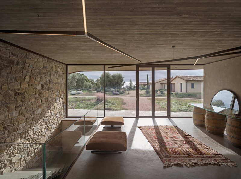 Interior tasting room with stone wall, timber ceiling, linear lighting, and glazed doors framing the landscape